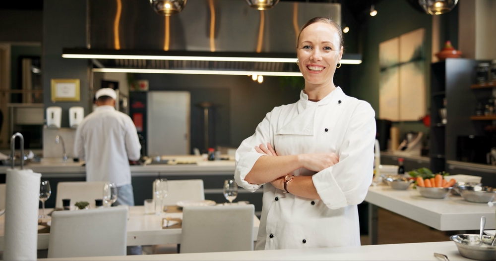 Woman Sous Chefsmi ling confidently in a modern commercial kitchen with high-spec catering equipment and open-plan layout.